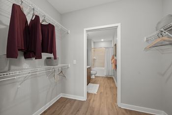 A white closet with clothes hanging and a mirror on the wall.